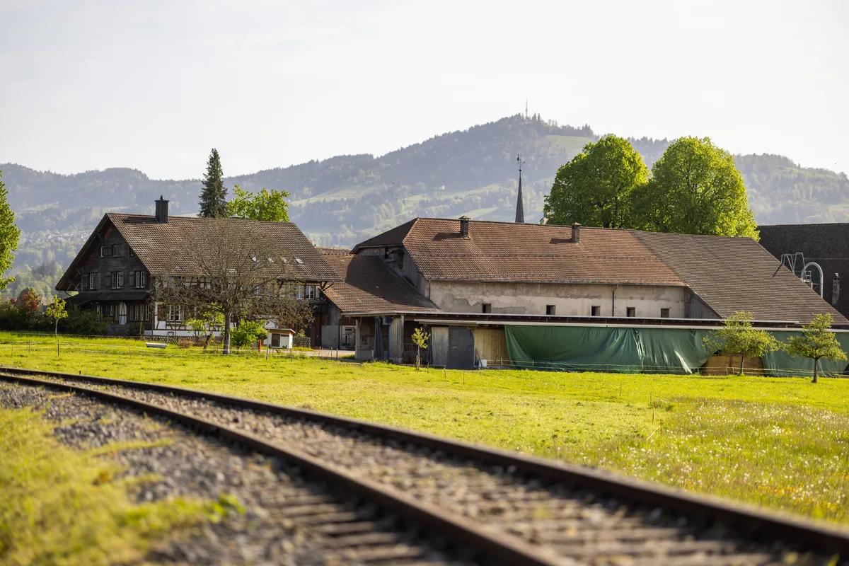 Blick auf den Ritterhaushof in Bubikon: Man sieht eine historische Scheune, ein Riegelhaus und im Vordergrund das alte Bahngleis der Uerikon-Bauma-Bahn.